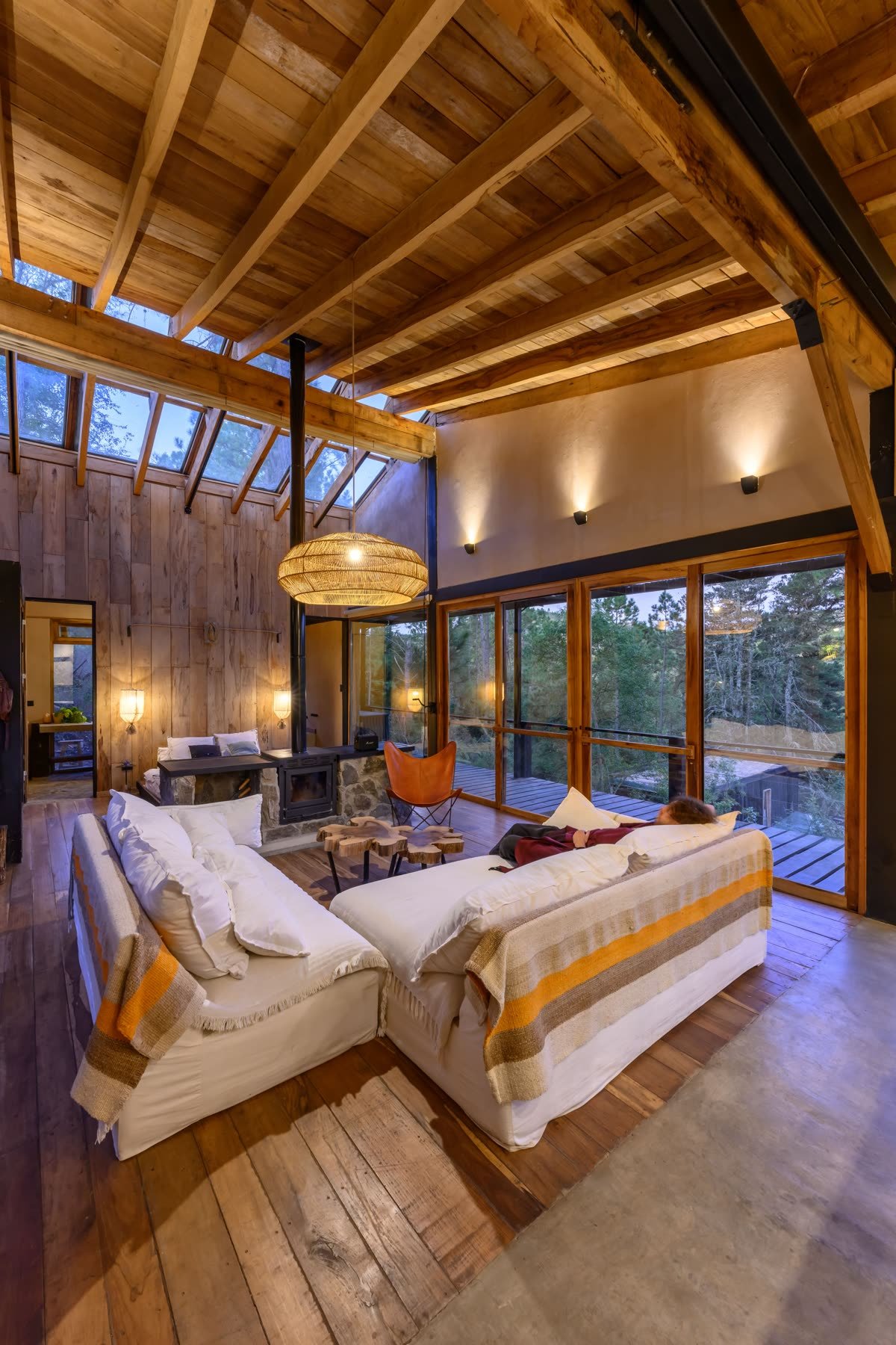 Interior de lodge wabi-sabi con lámparas de mimbre y ventanales al bosque